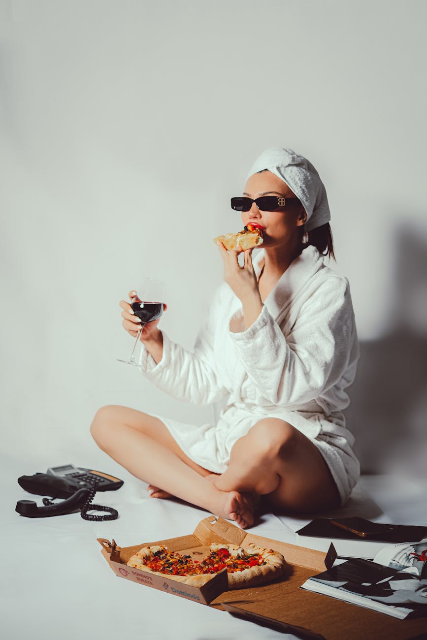 woman in robe enjoying pizza and wine indoors